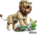 Gele lego leeuw met bruine manen, witte tanden en een groene, stenige omgeving met roze bloemen.