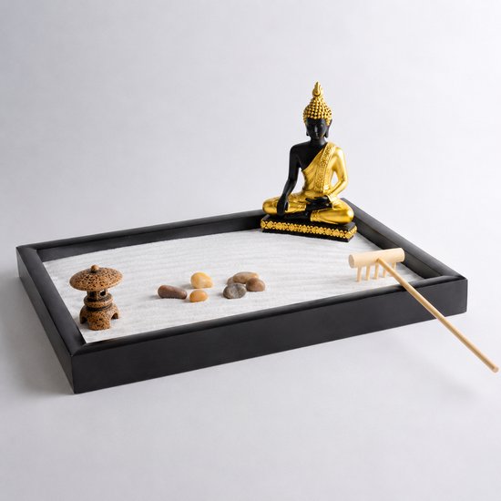 Plateau de jardin zen noir avec sable blanc, une statue de Bouddha noire et dorée assise, des pierres, un râteau en bois et une petite pagode.