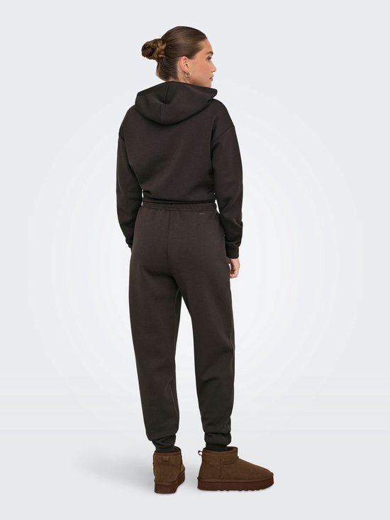 Model in een donkerbruine joggingbroek met trekkoord en capuchontrui.