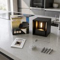 Zwarte kubusvormige wandlamp op een aanrecht, met verpakking en toebehoren.