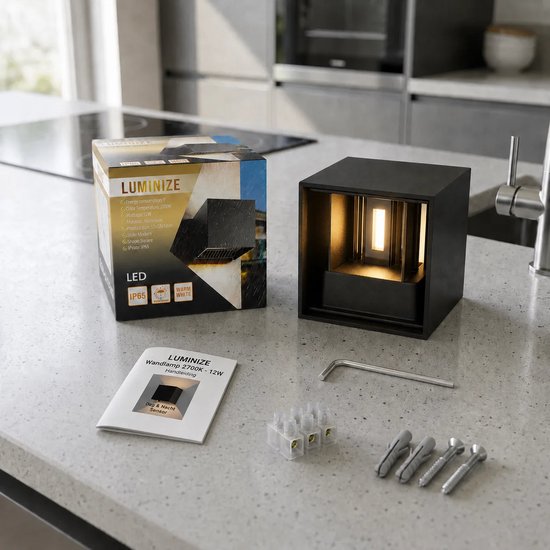 Zwarte kubusvormige wandlamp op een aanrecht, met verpakking en toebehoren.