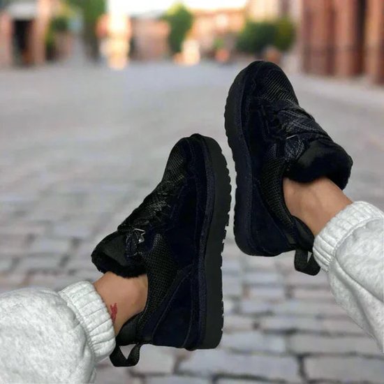 Damesvoeten met zwarte UGG sneakers met bontvoering, gedragen met een grijze joggingbroek.