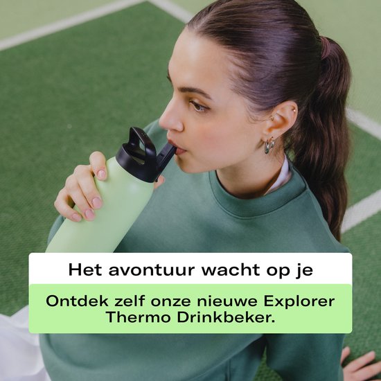Een vrouw met halflang bruin haar, gekleed in een groene trui, drinkt uit een lichtblauwe waterfles.