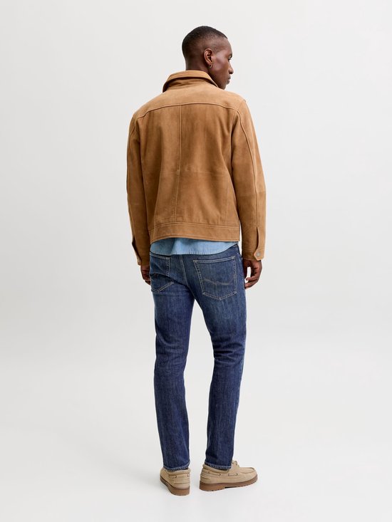 Man in een spijkerbroek, een blauw overhemd en een bruine jas, van achteren gezien.