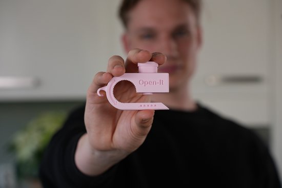 Man houdt lichtroze 'Open-It' opener vast, die tevens pillenbreker is.