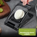 Hand plaatst ei in zwarte eiersnijder voor nauwkeurig snijden.