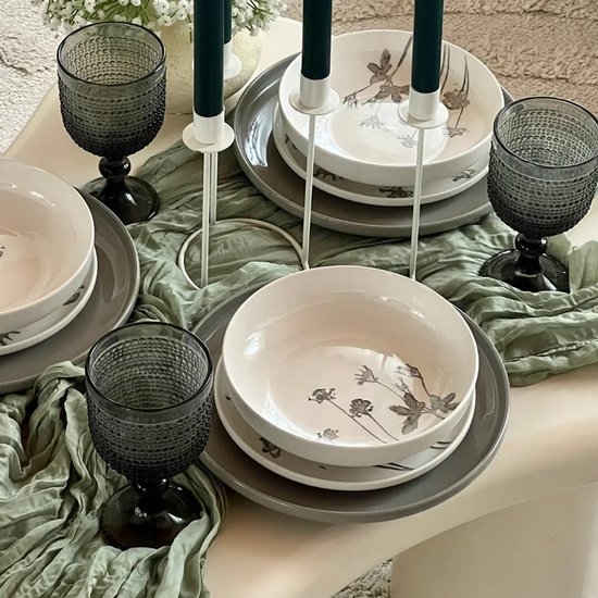 Drie donkergrijze glazen met bobbelig reliëf op een gedekte tafel met servies en kaarsen.