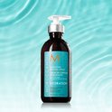 Moroccanoil Hydrating Styling Cream fles met pompdispenser. Turquoise label met oranje M-logo, omringd door waterdruppels.