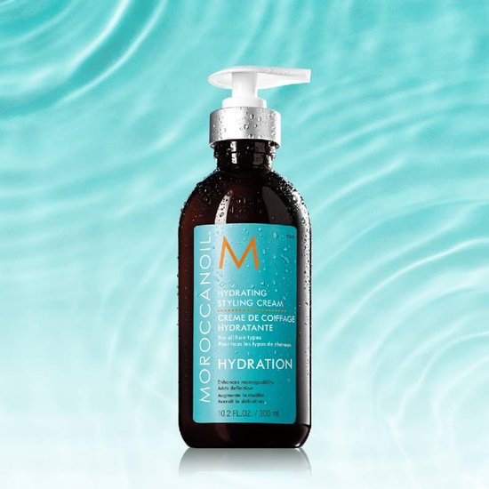 Moroccanoil Hydrating Styling Cream fles met pompdispenser. Turquoise label met oranje M-logo, omringd door waterdruppels.