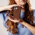 Vrouw met krullend rood haar houdt bruin telefoonhoesje met polkadots vast.