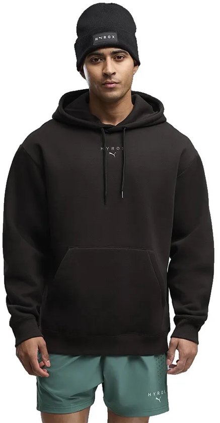 Man draagt een zwarte hoodie met het HYROX-logo op de borst, gecombineerd met een zwarte muts.