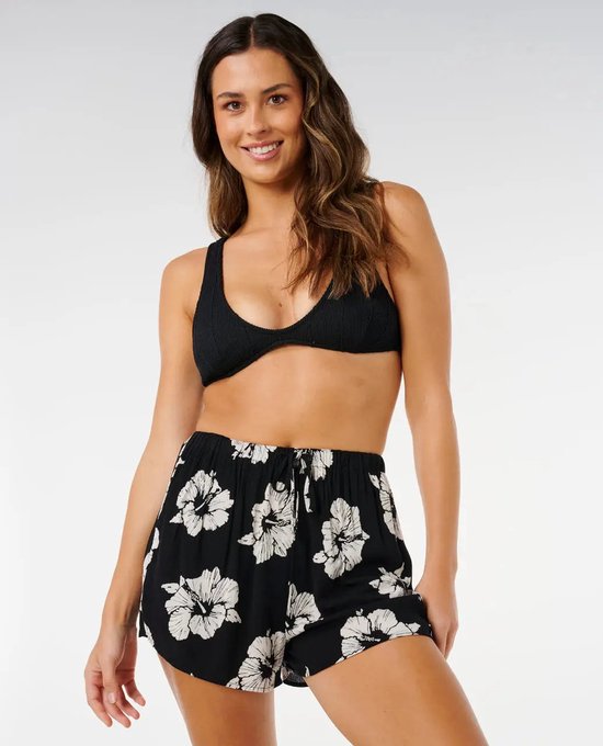 Model draagt korte zwarte broek met witte bloemenprint en zwart bikinibovenstuk.