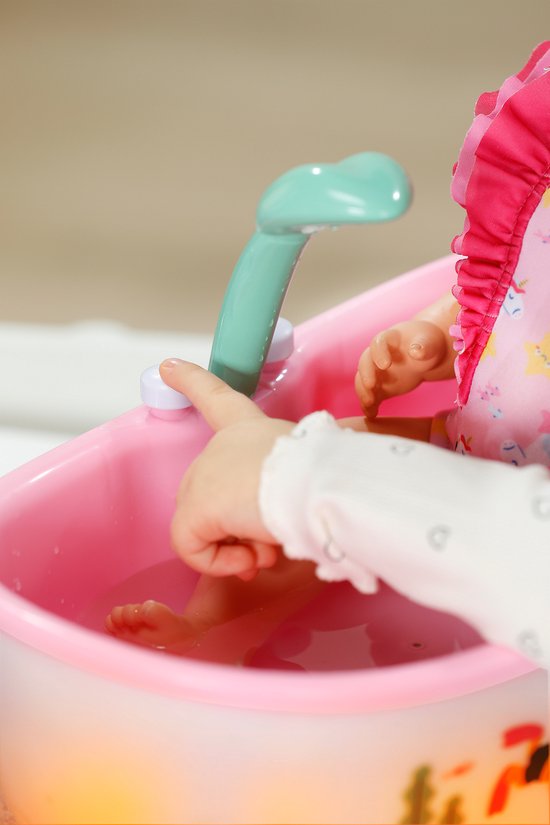 Kind duwt op de knop van het mintgroene douchekopje boven het roze babybadje.
