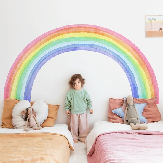 Un enfant se tient entre deux lits, avec un sticker arc-en-ciel en arrière-plan.