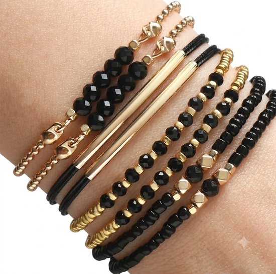 Set van 8 armbanden met zwarte kralen en gouden details, gedragen op een pols.