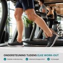 Een man traint op een loopband met lichte beige kuitcompressiemouwen, die tot net onder de knie reiken.