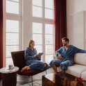Homme et femme en peignoirs bleus se détendent dans un salon, regardant une tablette et l'un l'autre.