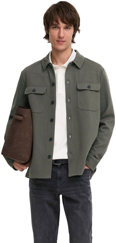 Mannelijk model met olijfgroene, lange mouwen oversized shirt, witte polo en grijze jeans.