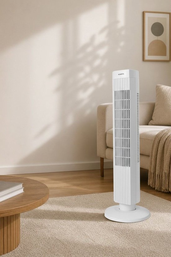 Witte staande ventilator van Kumtel in een sfeervol verlichte woonkamer, op een kleed voor een bank.