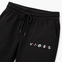 Detailopname van de 'VIBES' print op een zwarte joggingbroek.