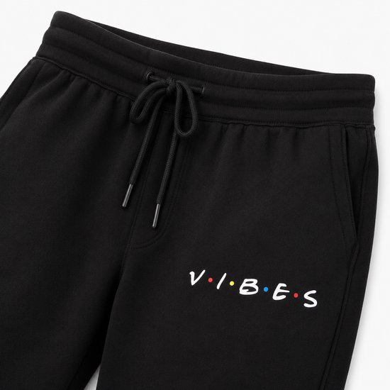 Detailopname van de 'VIBES' print op een zwarte joggingbroek.