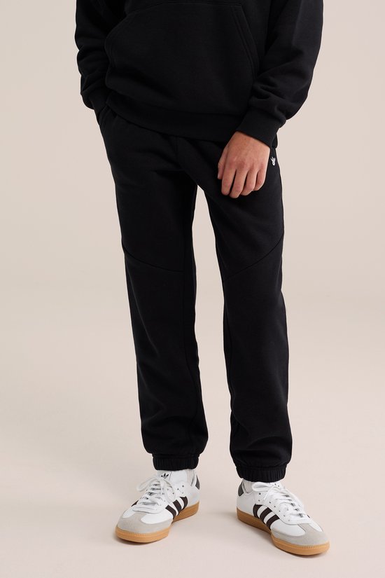 Zwarte joggingbroek met smalle boorden bij de enkels, gedragen met witte sneakers.