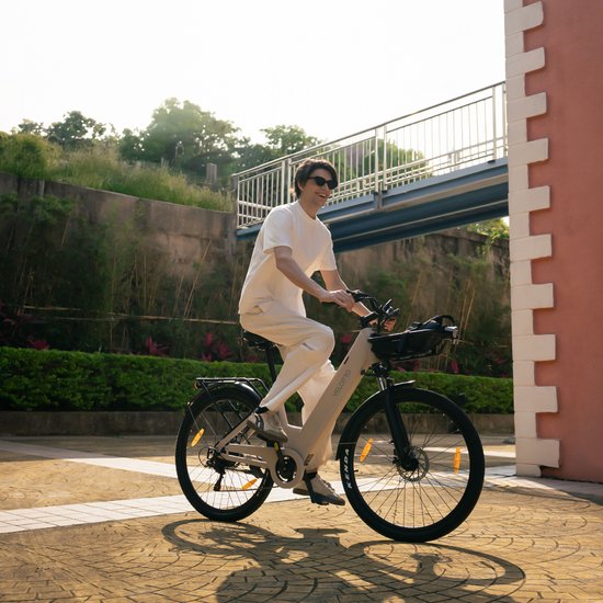 Man met witte kleding op een lichtgrijze elektrische fiets met mand voorop.