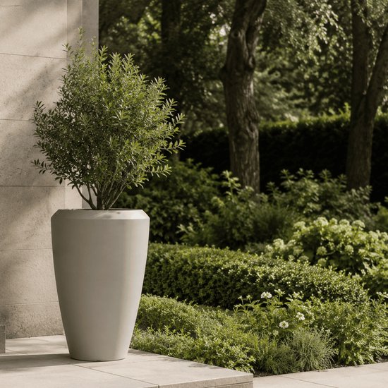 Jardinière conique gris clair avec un arbuste à feuilles persistantes, dans un jardin avec des dalles en pierre.