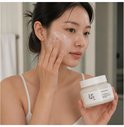 Vrouw brengt grondrijst- en honingmasker aan op haar gezicht, houdt potje van Beauty of Joseon vast.