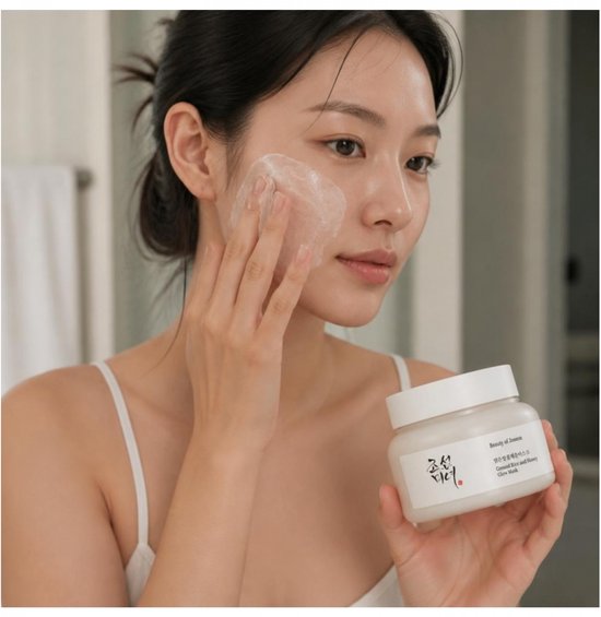 Vrouw brengt grondrijst- en honingmasker aan op haar gezicht, houdt potje van Beauty of Joseon vast.