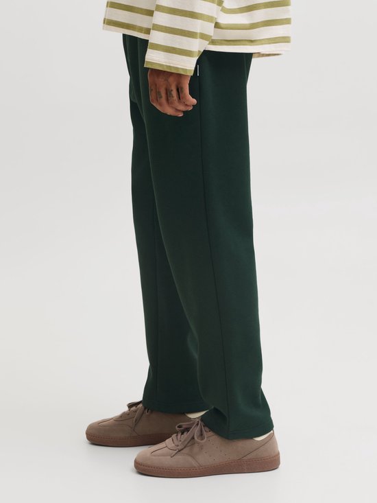 Detail van een donkergroene joggingbroek en bruine sneakers.