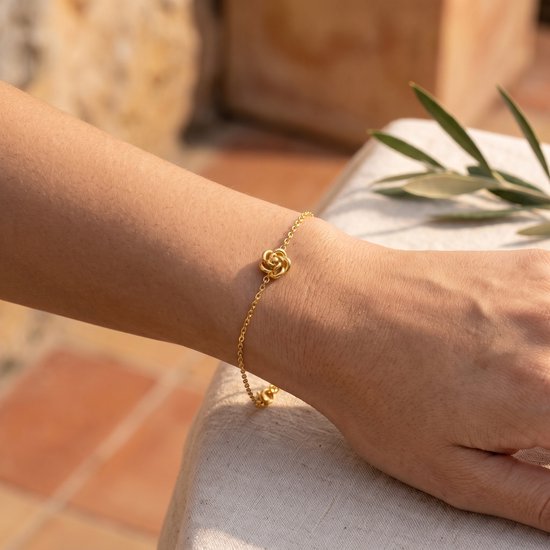 Gouden armband met een klein roosje, gedragen om een pols.