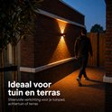 Man loopt langs een bakstenen huis met verlichte tuinpad, door wandlampen.