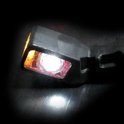 Zwarte LED-markeringslamp met een helder wit licht en oranje zijkant in een donkere omgeving.