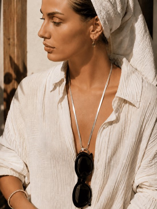 Mannequin avec une serviette sur la tête, porte une chemise blanche avec un collier argenté auquel est attachée une paire de lunettes de soleil noires.