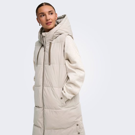 Model van opzij gezien in een lange, lichtgrijze gewatteerde bodywarmer met capuchon.