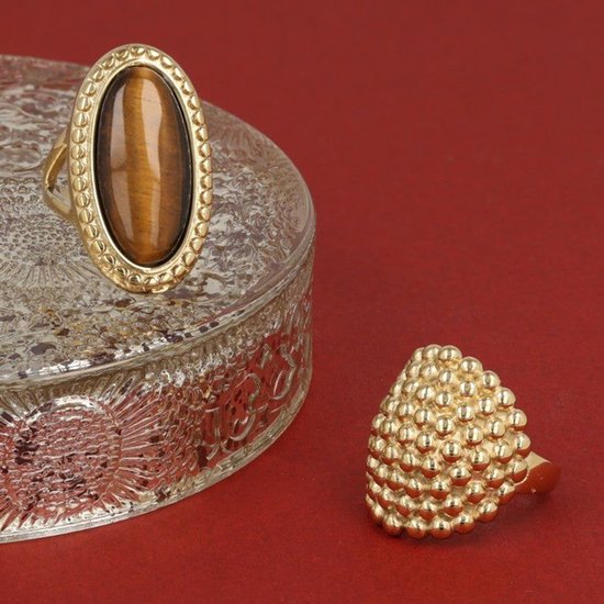 Gouden ringen, een met tijgeroog edelsteen op een glazen schaal, en een ring met gouden bolletjes.