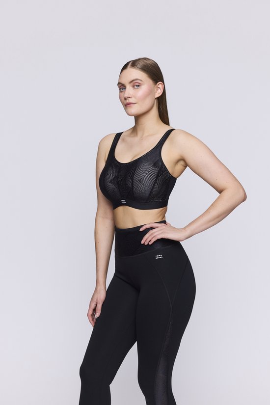 Model in een zwarte sportbeha van PrimaDonna met gestreepte cups en zwarte legging. Hand op de heup.