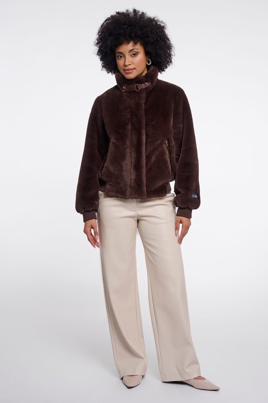 Een model draagt een bruine Faux Fur bomberjack met hoge kraag en leren sluitingen. Ze draagt een lichte broek.