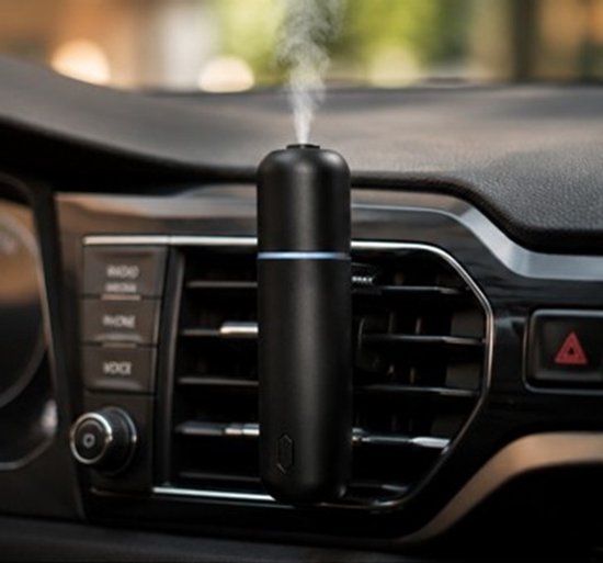 Zwarte aroma diffuser met blauwe gloed, geplaatst in een auto-ventilatiesysteem en stoom komt uit de bovenkant.