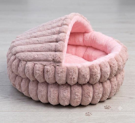 Un lit doux pour chat ou chien rose avec un motif côtelé et un toit couvert, sur un plancher en bois.