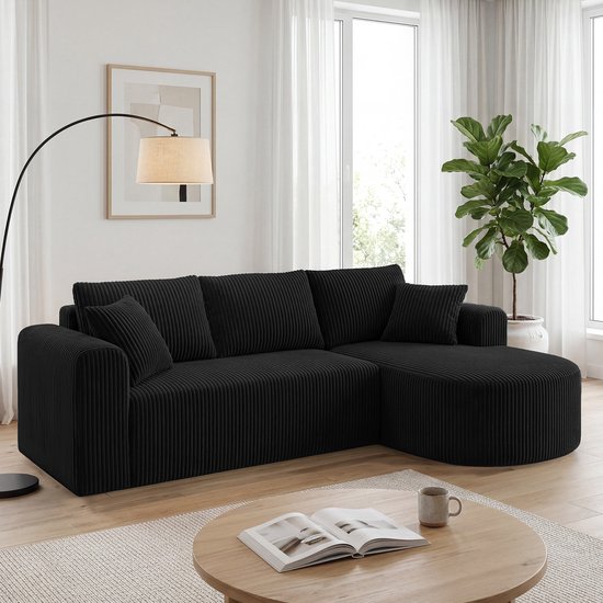 Canapé d'angle noir en velours côtelé, confortablement installé dans un salon avec une table basse et un lampadaire.