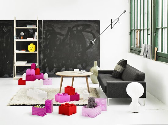 Een woonkamer met een donkergrijze bank, een salontafel en rode, roze en witte Lego-opbergdozen op een vloerkleed.