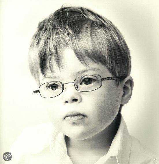 Een jongen met kort bruin haar en een bril, draagt een wit shirt. Zwart-wit foto.