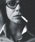 Close-up van een vrouw met bril en sigaret in haar mond. Zwart-wit.
