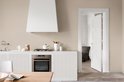 Keuken met witte keukenkastjes, gasfornuis en een open deur naar woonkamer.