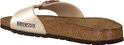 Zijaanzicht van een parelmoer witte Birkenstock slipper met een koperkleurige gesp en kurken zool.