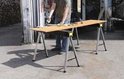 Man gebruikt twee inklapbare zaagbokken met een houten plank erop als werktafel.