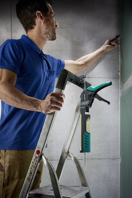Man op een ladder gebruikt een wolfcraft kitpistool met groene en zwarte accenten om een muur af te werken.