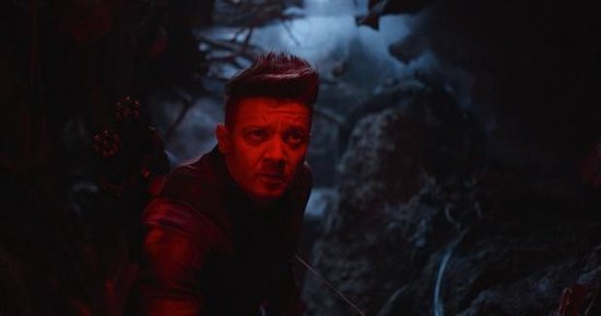 Hawkeye in rood licht, met pijlkoker, kijkt geconcentreerd.